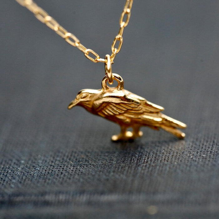 Gold bird-shaped pendant on a chain against a dark fabric background