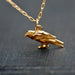 Gold bird-shaped pendant on a chain against a dark fabric background