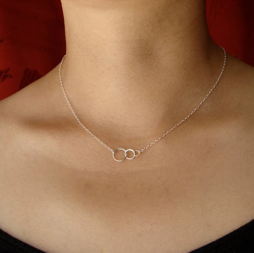 Silver necklace with a double circle pendant on a person's neck against a red background
