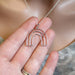 Hand holding a silver necklace with a rainbow pendant against a neutral background
