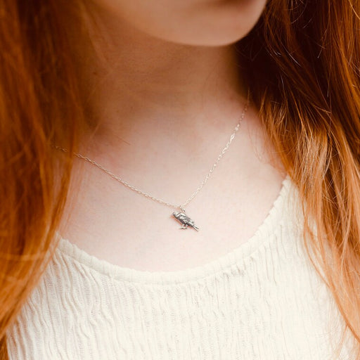 Person with long red hair wearing a delicate necklace with a small pendant.
