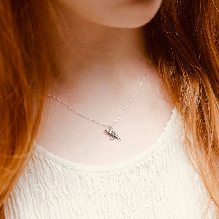 Person with long red hair wearing a delicate necklace with a small pendant.