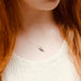 Person with long red hair wearing a delicate necklace with a small pendant.