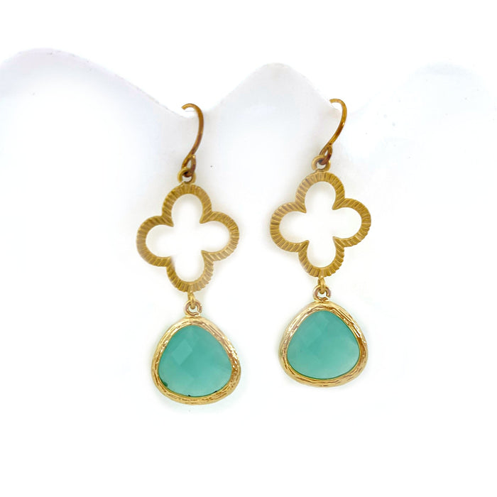 A pair of gold-plated clover earrings with faceted aquamarine glass charms attached to them, displayed against a white background.