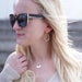 lady wearing a neutral v neck sweater wearing sunglasses and gold crystal earrings and a gold necklace