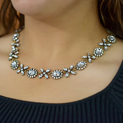 A close-up of a woman wearing a silver-toned floral crystal necklace over a dark ribbed top.