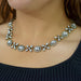 A close-up of a woman wearing a silver-toned floral crystal necklace over a dark ribbed top.