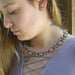 A close-up lifestyle shot of a woman wearing a silver-toned floral crystal necklace and matching stud earrings, wearing a lavender top.
