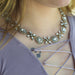 A close-up lifestyle shot of a woman wearing a silver-toned floral rhinestone collar necklace over a lavender top.