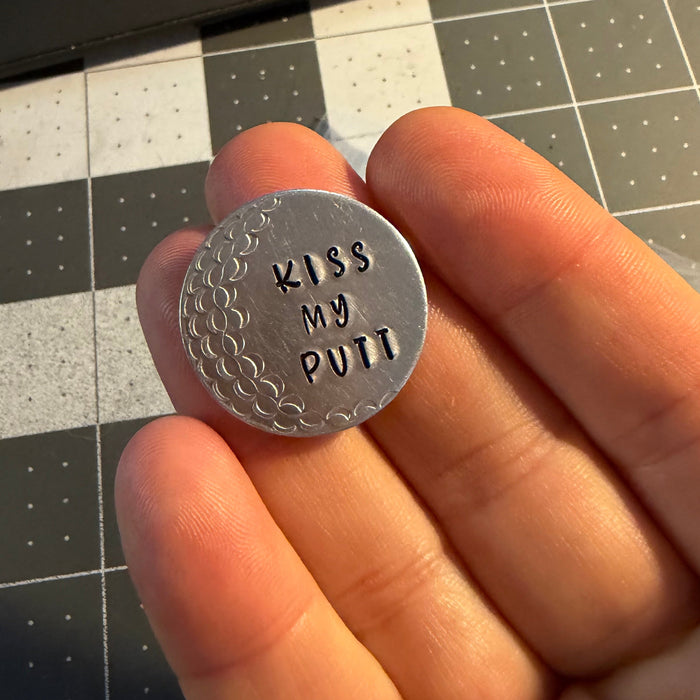 Hand holding a small silver coin with text on a grid background