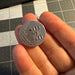 Hand holding a small silver coin with text on a grid background