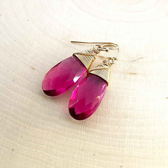 A pair of pink tourmaline quartz earrings with 14k gold fill wire hand-wrapping, displayed on a textured background.