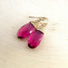 A pair of pink tourmaline quartz earrings with 14k gold fill wire hand-wrapping, displayed on a textured background.