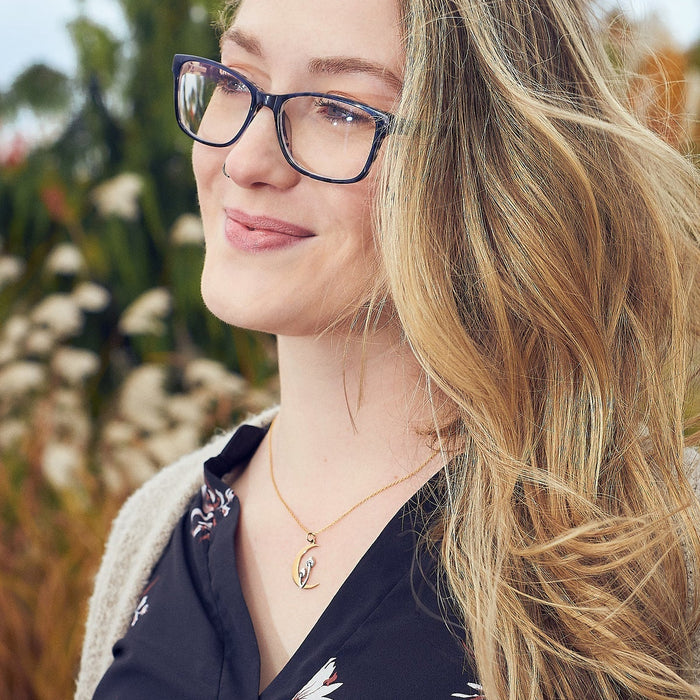 Woman with glasses and long blonde hair standing outdoors with blurred natural background