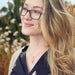 Woman with glasses and long blonde hair standing outdoors with blurred natural background