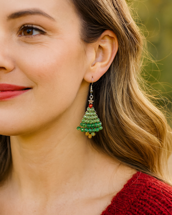 Close-up of a woman wearing a green Christmas tree earring with a blurred outdoor background