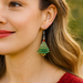 Close-up of a woman wearing a green Christmas tree earring with a blurred outdoor background