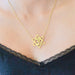 Gold necklace with a geometric pendant worn by a person in black lingerie.