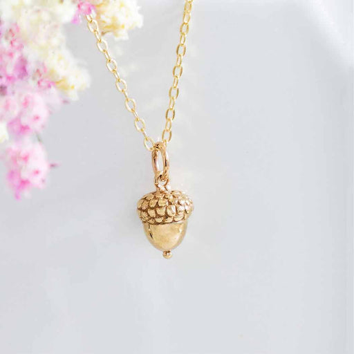 close up view of a gold acorn charm hanging from a gold chain