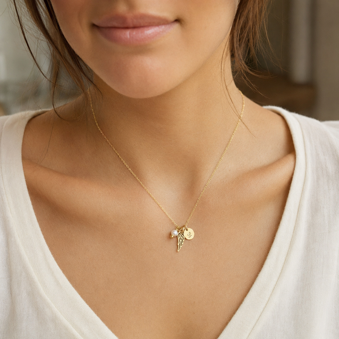 Woman wearing a personalized 14k gold filled angel wing memorial necklace with freshwater pearl and hand-stamped initial