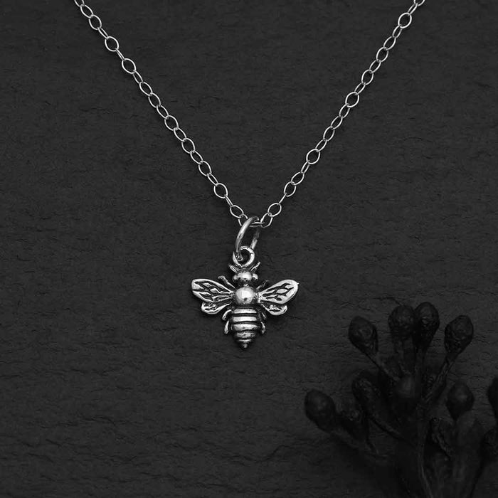 close up view of a sterling silver bee pendant hanging from a silver cable chain on a solid black background