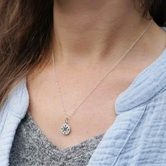 view of a model's neck wearing a silver necklace with a small compass circle charm