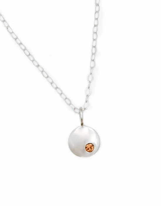 Close-up of sterling silver disc necklace with orange Swarovski birthstone on white background.
