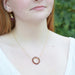 a gold necklace with a circle wire wrapped with garnet gemstones shown on a fair skinned model in white shirt with red hair