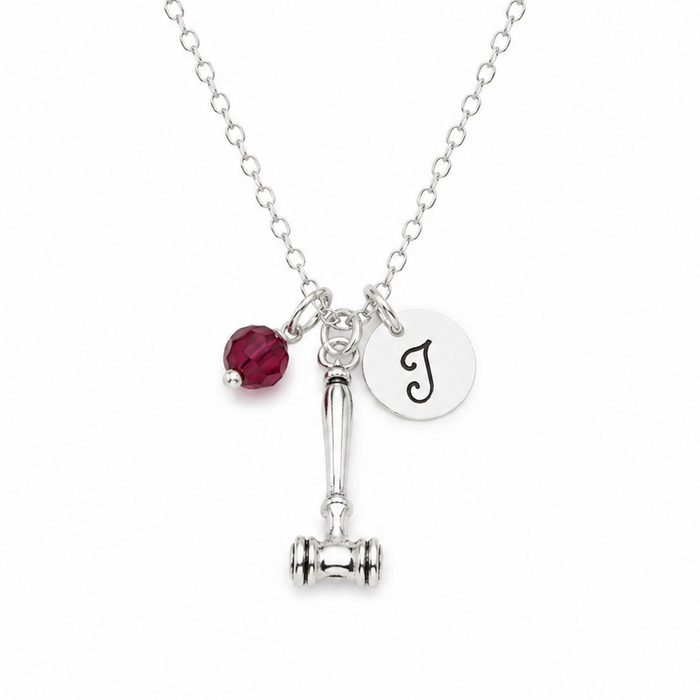 Necklace with a red bead, gavel charm, and round initial pendant on a white background