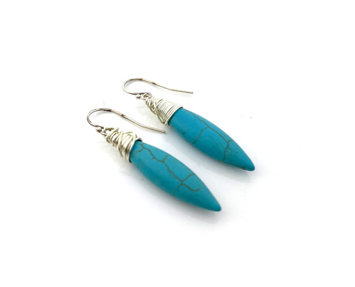 The earrings feature elongated, marbled turquoise stones wrapped in delicate silver wire, suspended from silver ear hooks.