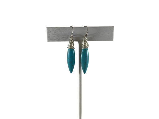 White leather earrings stand with earrings. The earrings feature elongated, marbled turquoise stones wrapped in delicate silver wire, suspended from silver ear hooks.