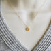Gold necklace with a round pendant on a gray sweater