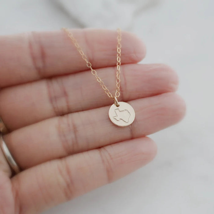 close up of a hand holding a gold filled texas state necklace to showcase size