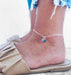 Silver anklet with single blue Swarovski charm, worn on ankle with sandals and jeans.