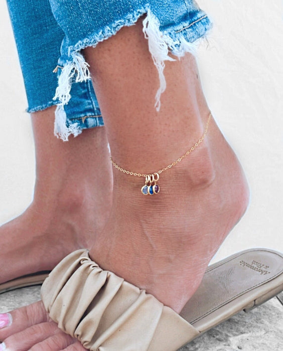 Adjustable silver birthstone anklet with personalized charms, styled on a barefoot model.

