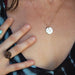 Close-up of a person wearing a necklace with a circular pendant, holding their hand near their neck.