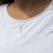 Person wearing a delicate gold necklace with a crescent moon pendant on a white shirt.