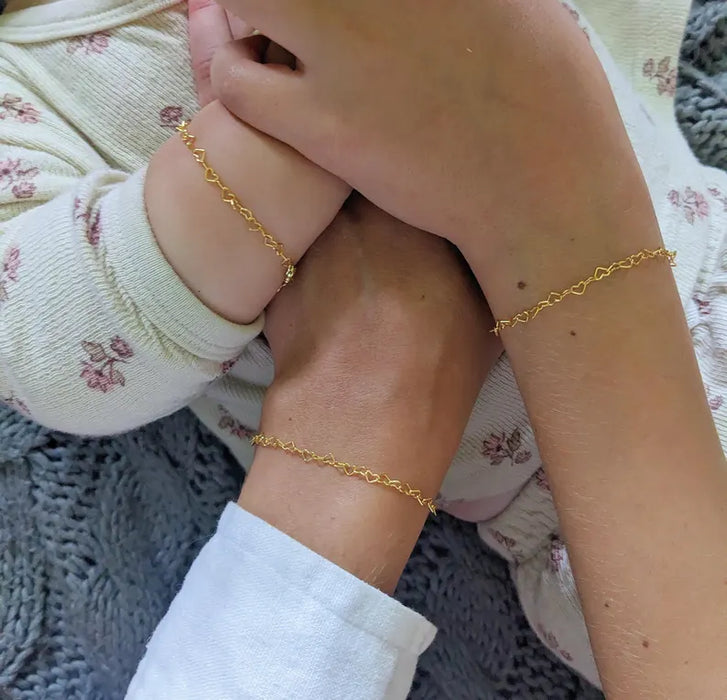 Two hands wearing gold bracelets on a textured fabric background