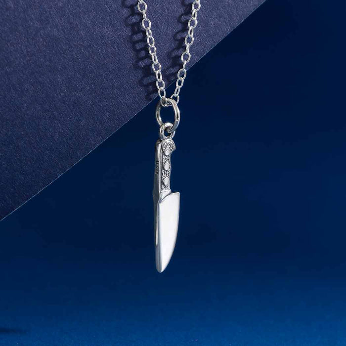 close up detail of sterling silver knife charm on chain on blue background