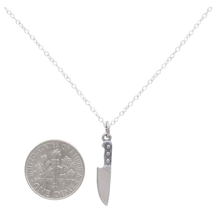 Sterling silver knife necklace next to s USD dime to compare size on a white background