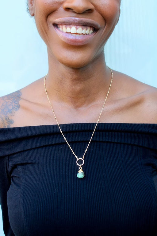 a flashing labradorite necklace in 14k gold on a beautiful dark skinned model's shoulders with her beautiful smile. 