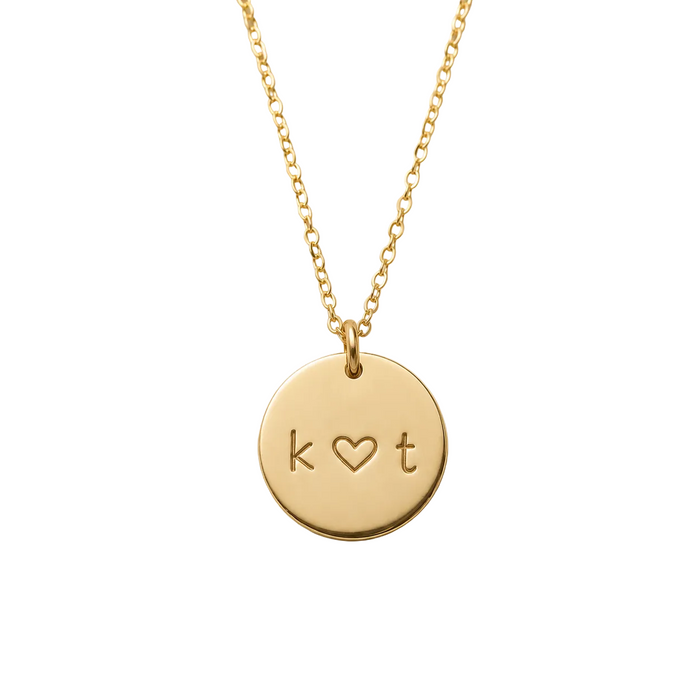 Gold necklace with a round pendant featuring 'k ❤️ t' on a beige background