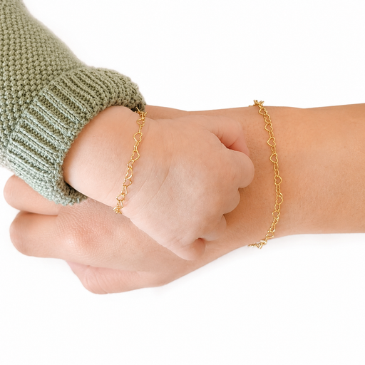 Two hands wearing gold heart bracelets on a white background