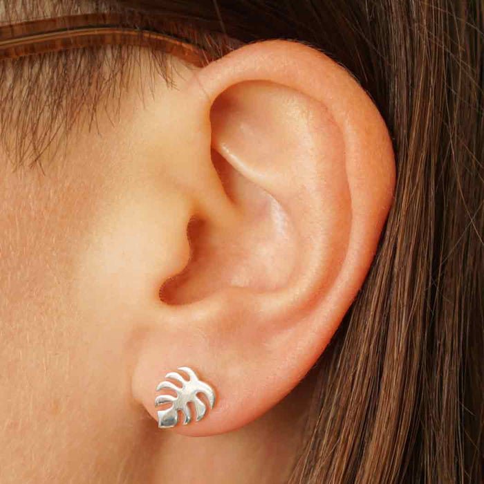 close up view of silver monstera post earring on model's ear