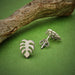 view of front and back of silver monstera leaf post earrings with wooden branch on green background