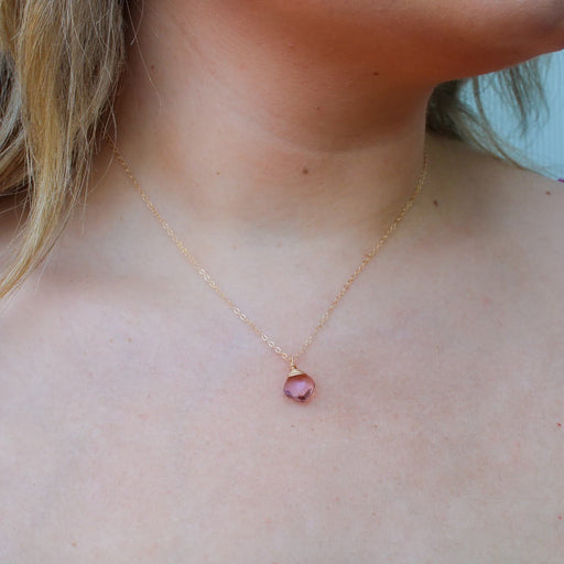 a view of a light skinned lady's neck with blonde hair and a pink blouse wearing a handmade gold necklace with a pink briolette