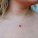 a view of a light skinned lady's neck with blonde hair and a pink blouse wearing a handmade gold necklace with a pink briolette