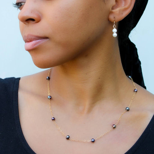 a profile view of a young lady in a black blouse wearing a peacock freshwater pearl satellite gold necklace