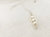 silver wire wrapped freshwater pearl peapod necklace on a neutral fabric texted background