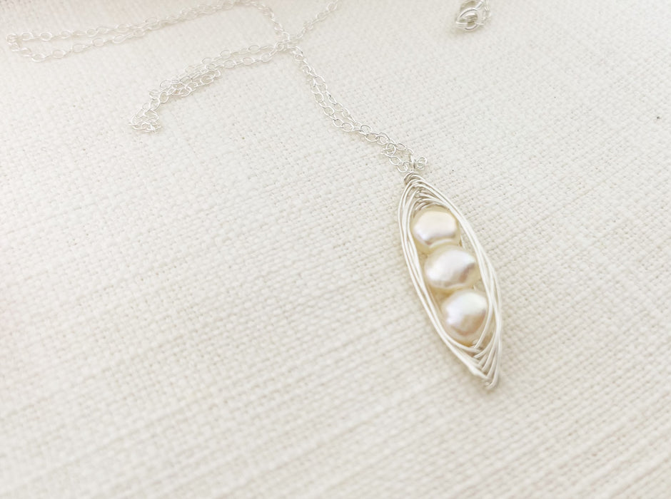 silver wire wrapped freshwater pearl peapod necklace on a neutral fabric texted background